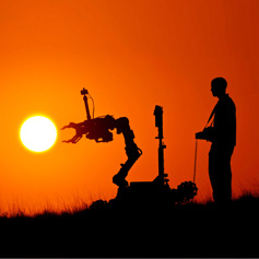 Man operating a robotic vehicle silhouetted against a sunset sky.