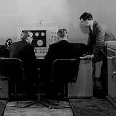 Black and white image of Alan Turing and others in a computer laboratory