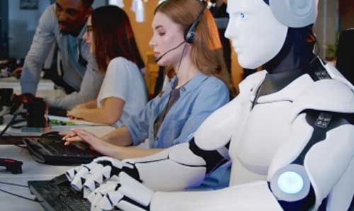 Robot sitting alongside humans typing on computers 