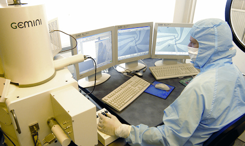 Researcher operating nanoscience equipment and looking at three monitors